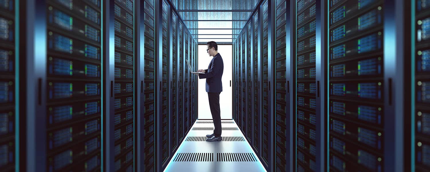 Man working on laptop inside a large server room