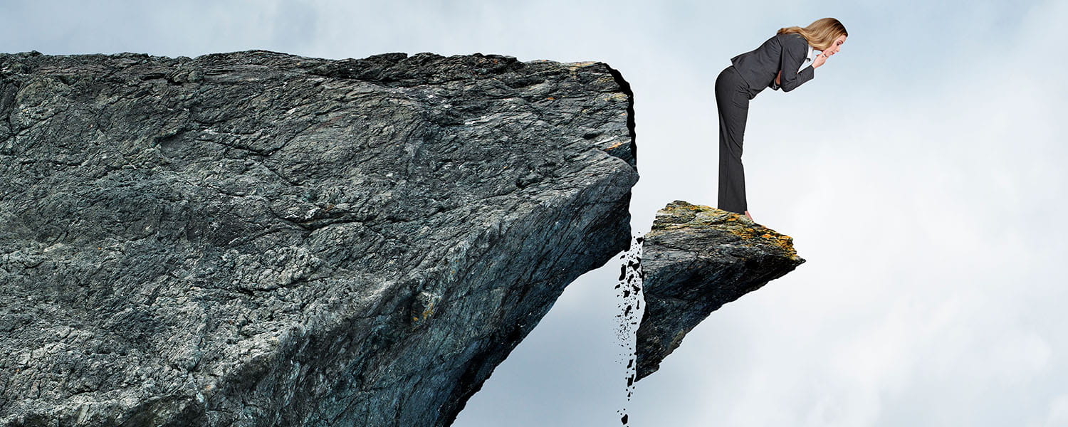 Woman standing on broken off edge of a cliff looking down as it falls